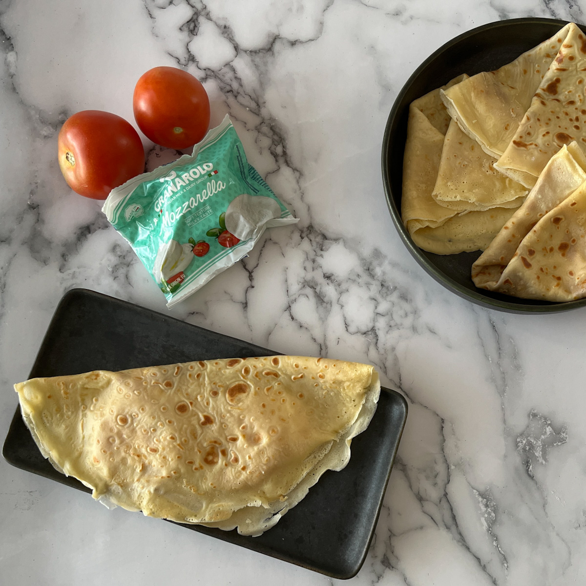 3-ingredient Crepes 2 crepe with mozzarella and tomatoes on a dark tray, mozzarella, two tomatoes and empty crepes on a dark plate